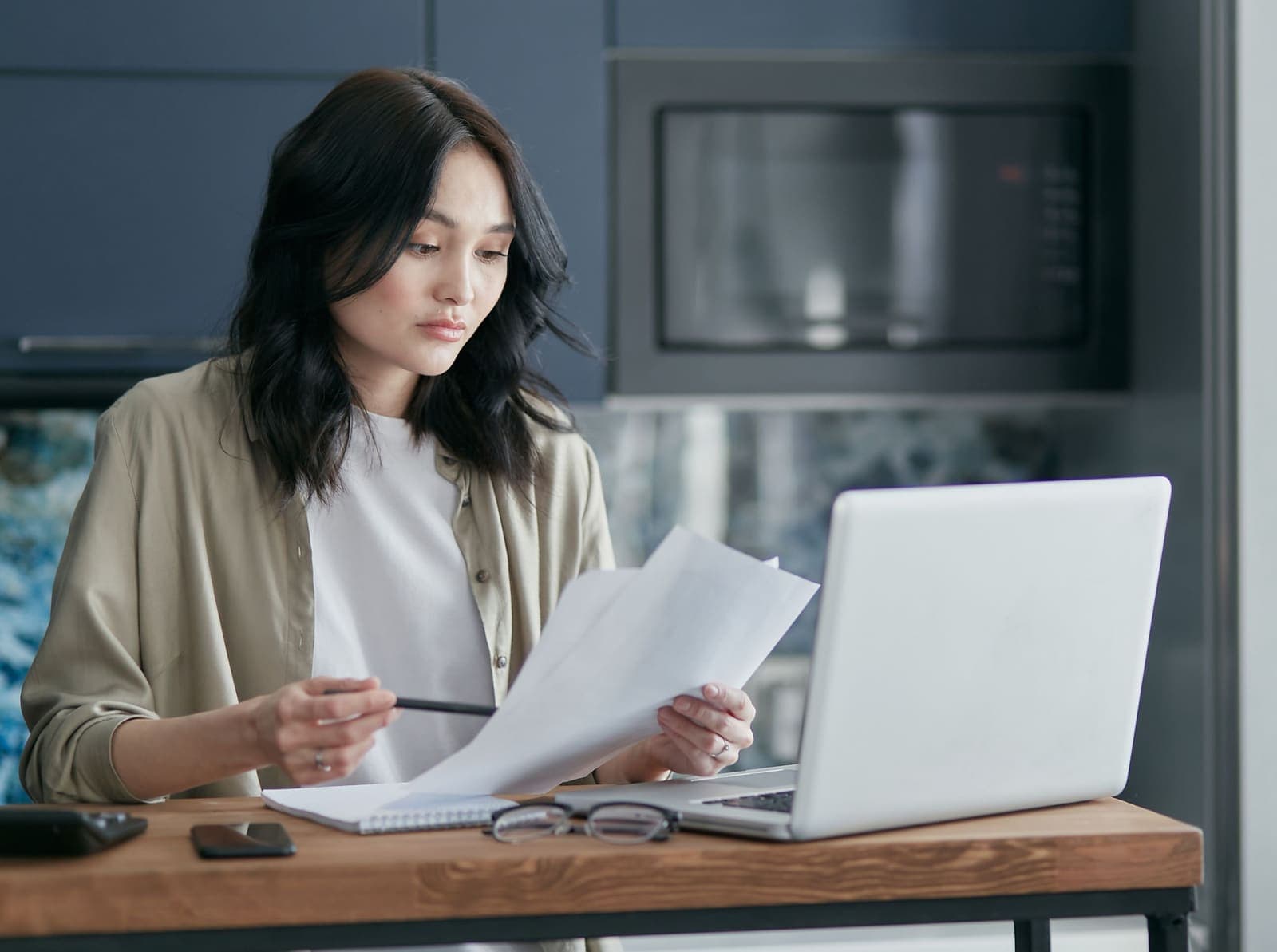A woman reviewing documents beside a laptop at her kitchen table